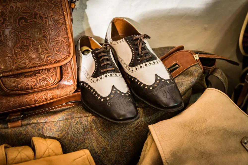 Zweifarbige Budapester Schuhe mit Brogue-Lochung neben Lederaccessoires