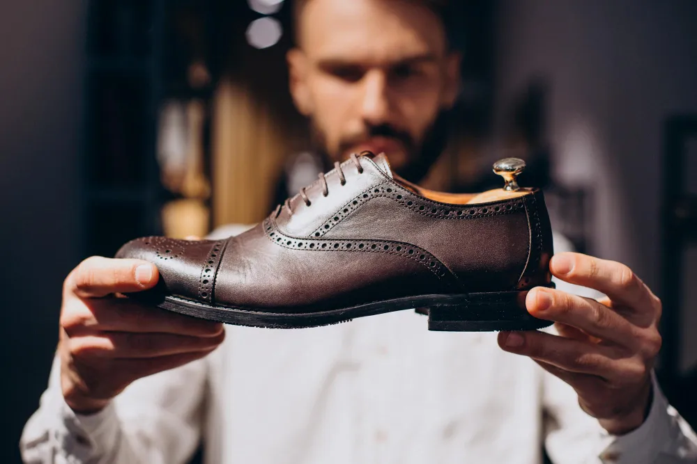 Mann hält dunkelbraunen Budapester Schuh mit Brogue-Lochung in den Händen
