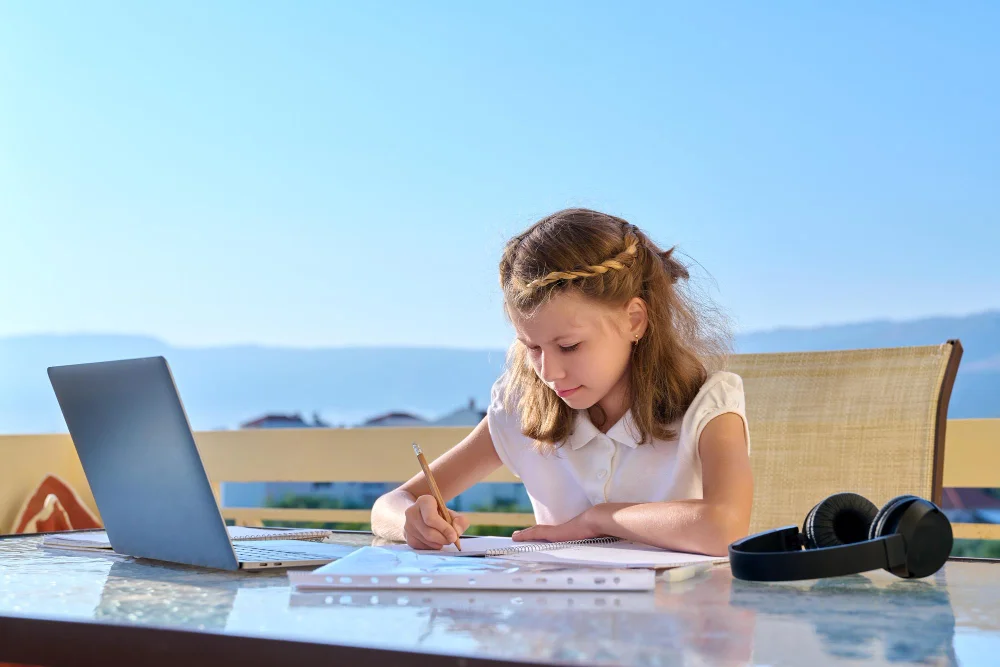 Kind lernt mit Laptop und Schulheft während einer Reise