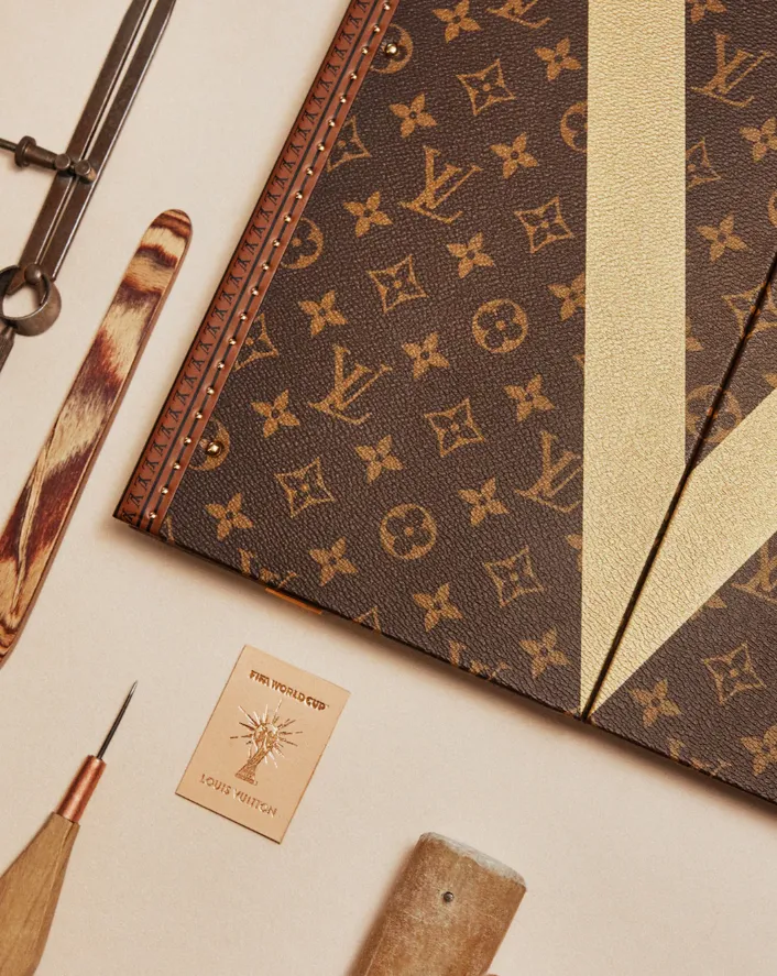 Detailaufnahme eines Louis-Vuitton-Koffers mit Monogramm, cremefarbenem V-Motiv und Werkzeugen zur handwerklichen Fertigung