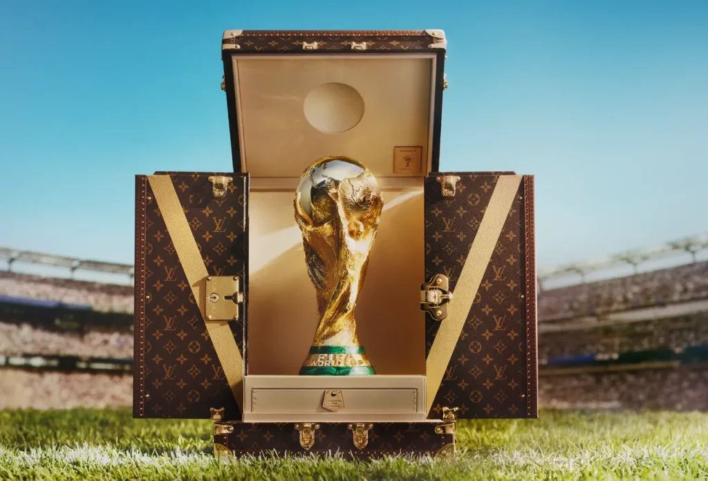 Der WM-Pokal 2026 steht in einem geöffneten Louis-Vuitton-Trophäenkoffer auf dem Rasen eines Fußballstadions.
