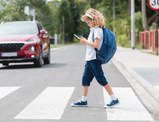 Ein Kind mit Schulranzen und Smartphone an einer Straße