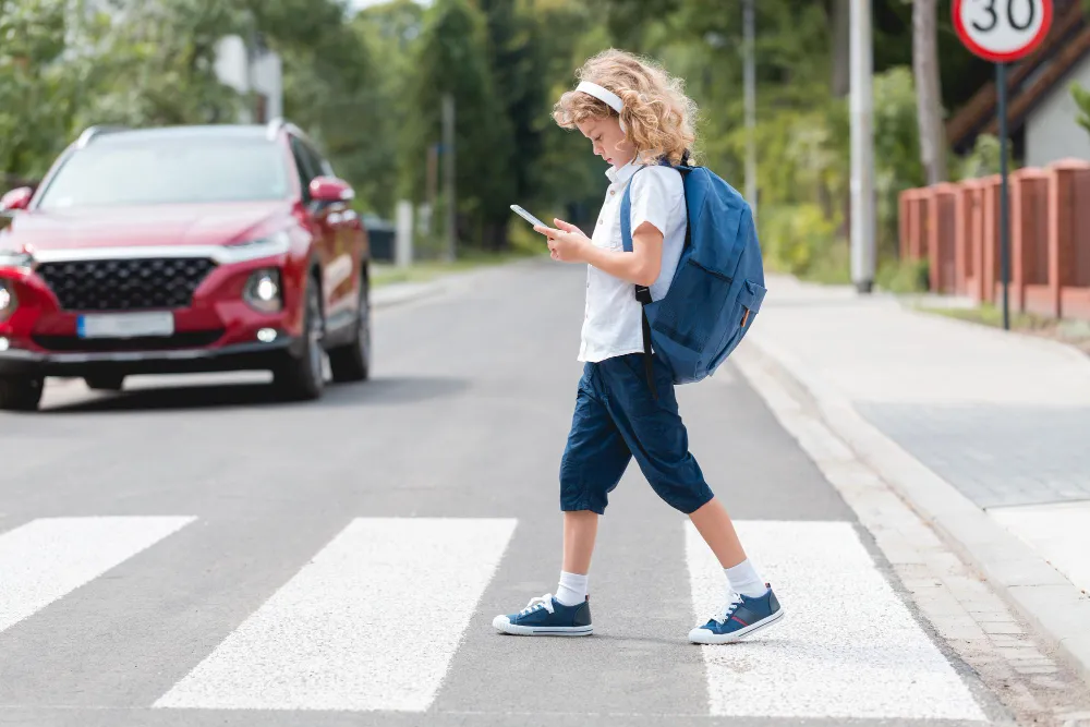 Ein Kind mit Schulranzen und Smartphone an einer Straße