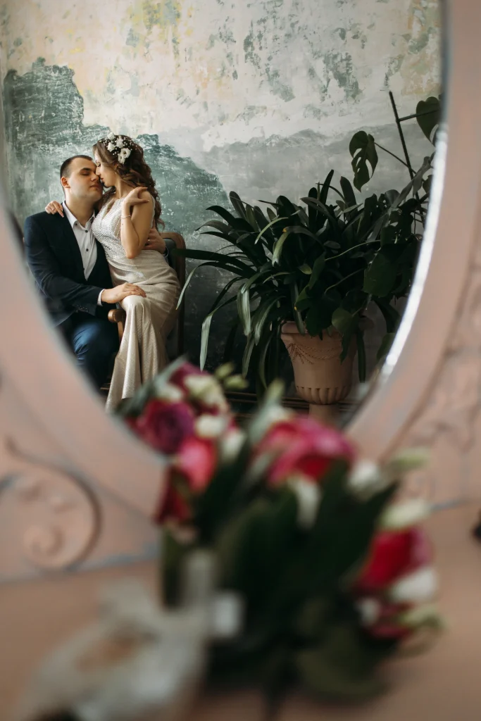 Braut und Bräutigam sitzen eng umschlungen in einem ruhigen Raum, gespiegelt im runden Spiegel – intime Hochzeitsfotografie mit natürlichem Licht