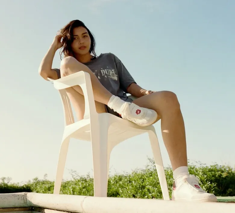 Frau sitzt draußen auf einem weißen Stuhl und trägt weiße Duke + Dexter Sneaker