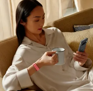 Frau trägt Google Fitbit Air Armband und blickt auf ihr Smartphone