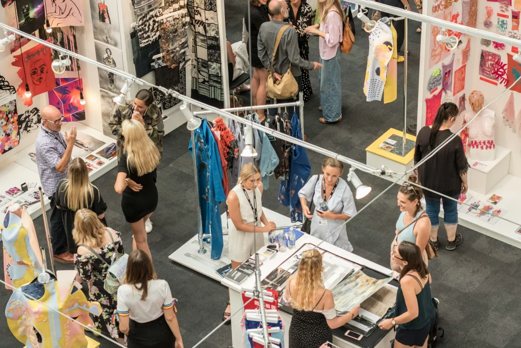 Besucherinnen und Besucher auf einer Modemesse mit Ständen für unabhängige Designer und nachhaltige Kleidung