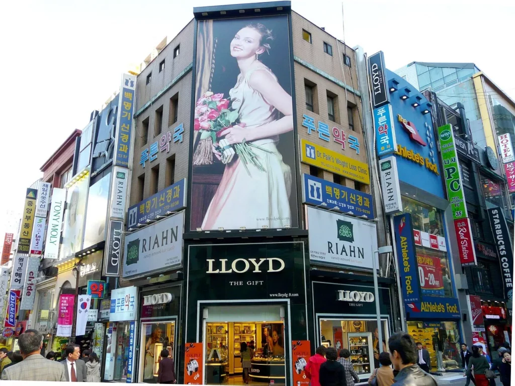 Geschäftsstraße mit großen Modegeschäften und Werbetafeln in einer asiatischen Metropole – Symbol für Fast Fashion und globalisierten Modekonsum.