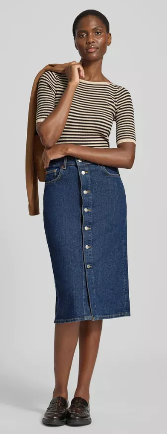 Frau trägt Midi-Jeansrock Outfit 2025 – blauer Denimrock mit Knopfleiste kombiniert mit gestreiftem Shirt, braunem Blazer und Loafern.