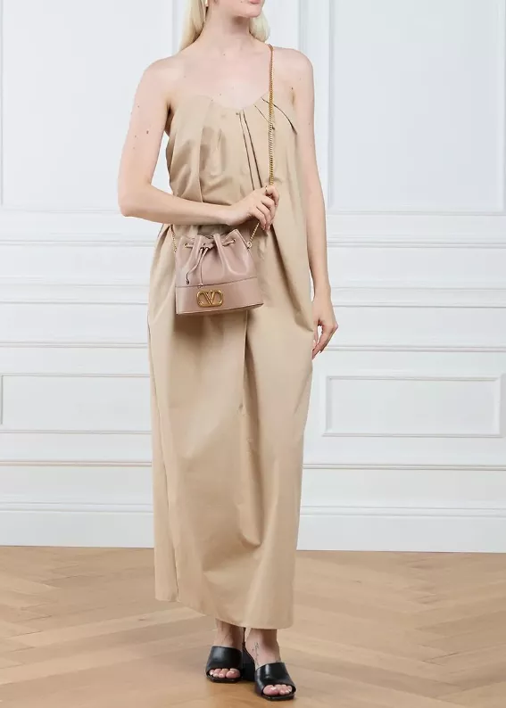 Frau trägt eine beige Bucket Bag von Valentino im Alltag, kombiniert mit einem eleganten Jumpsuit in Beige und schwarzen Sandalen.