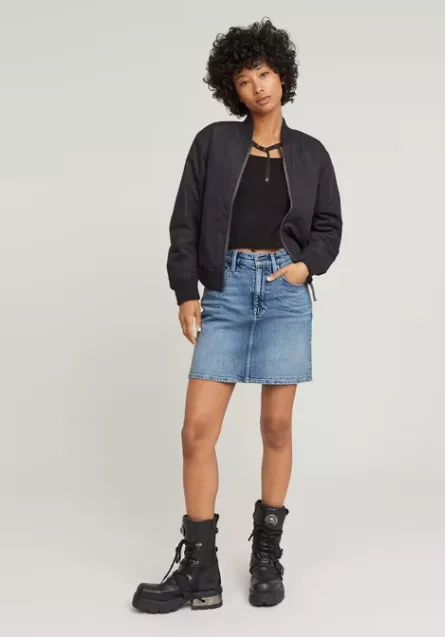 Frau trägt Jeansrock Outfit 2025 – blauer Denimrock, schwarzes Top, Bomberjacke und Boots im Streetstyle-Look.