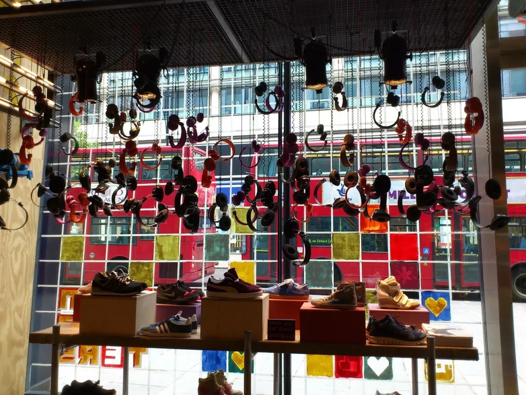 Sneaker-Auslage in einem modernen Schaufenster mit bunten Kopfhörern und Blick auf rote Doppeldeckerbusse in der Stadt.