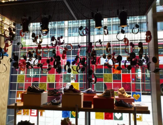 Sneaker-Auslage in einem modernen Schaufenster mit bunten Kopfhörern und Blick auf rote Doppeldeckerbusse in der Stadt.