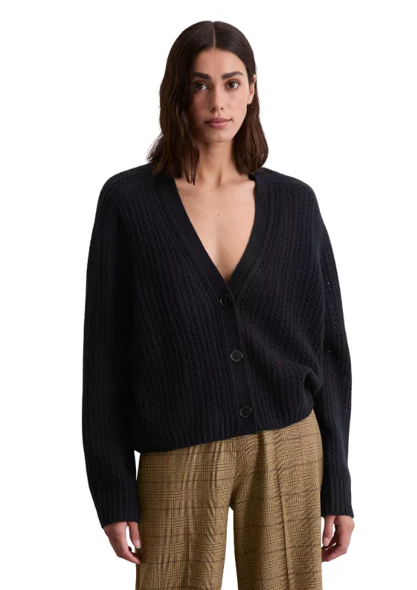Cardigan vs. Strickjacke – Frau trägt schwarzen Damen-Cardigan mit Knopfleiste und weitem V-Ausschnitt zu karierter Hose