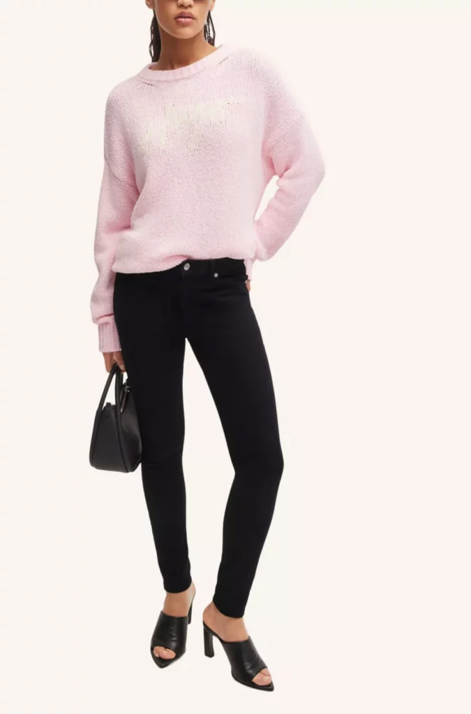Frau trägt schwarze Skinny Jeans Damen mit rosa Pullover und schwarzen High-Heel-Sandalen – Outfit-Trend 2025