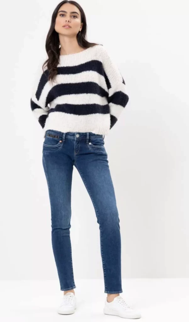 Frau trägt blaue Skinny Jeans Damen mit gestreiftem Pullover und weißen Sneakers – lässiger Trendlook 2025