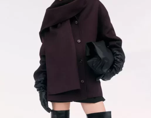 Mantel Damen bordeaux – kurzer Wollmantel mit Oversize-Schal, schwarze Lederhandschuhe und Overknee-Stiefel zu Minirock/Shorts vor hellem Hintergrund.