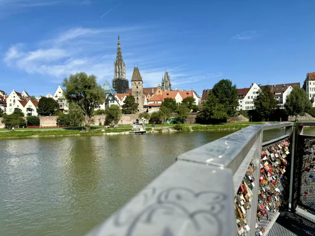 Blick über die Donau auf die Altstadt von Ulm mit dem Ulmer Münster im Hintergrund, fotografiert von Neu-Ulm mit Liebesschlössern im Vordergrund.