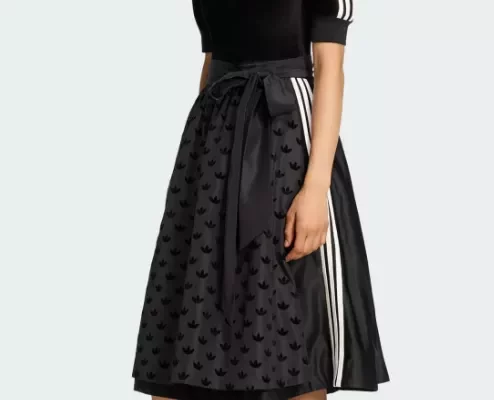 Frau trägt das adidas Dirndl in Schwarz mit dezenten weißen Streifen, Schürze mit Allover-Logo und sportlicher Silhouette.