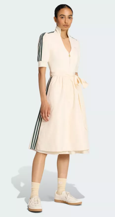 Frau trägt das adidas Dirndl in Chalk White mit Stehkragen, Reißverschluss und dezenten drei Streifen auf Ärmel und Schürze.