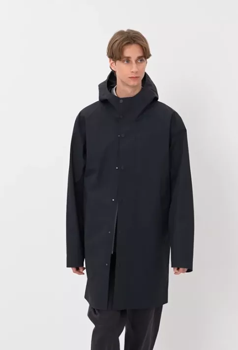 Mantel Herren schwarz mit Kapuze – minimalistischer, wasserabweisender Tech-Mantel mit verdeckter Knopfleiste und gerader Silhouette vor hellem Hintergrund.