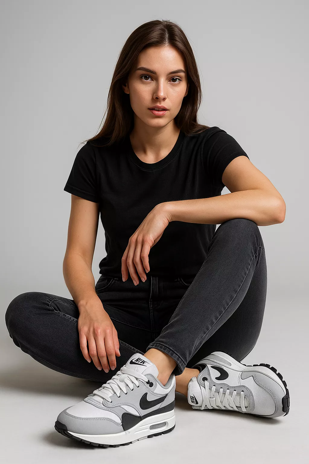 Model sitzt in grauen Skinny Jeans mit schwarzen Nike Sneakern und schwarzem T-Shirt – urbaner Denim-Trend 2025