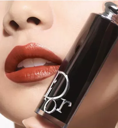 Dior Lippenstift – Close-up mit glänzendem Ziegelrot auf den Lippen; daneben die schwarze Dior Addict Hülse mit vertikalem Dior-Schriftzug und silbernem Kopf.