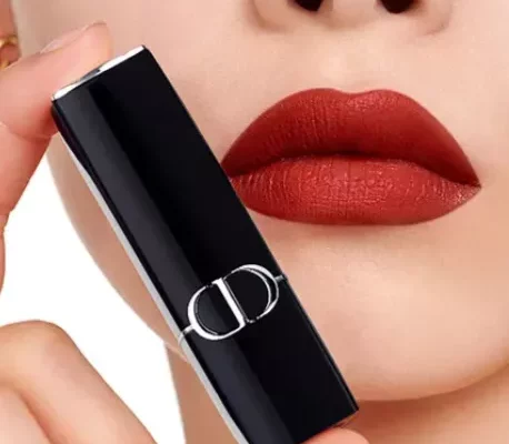 Dior Lippenstift – Nahaufnahme mit samt-matten ziegelroten Lippen; daneben hält eine Hand die schwarze Hülse mit silbernem CD-Logo.