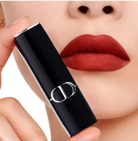 Dior Lippenstift – Nahaufnahme mit samt-matten ziegelroten Lippen; daneben hält eine Hand die schwarze Hülse mit silbernem CD-Logo.