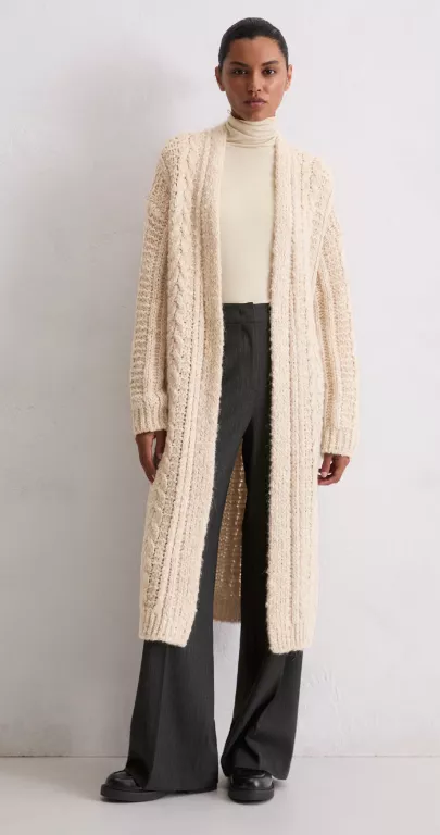 Cardigan vs. Strickjacke – Frau trägt lange beige Strickjacke im Maxi-Cardigan-Stil über Rollkragenpullover und Stoffhose