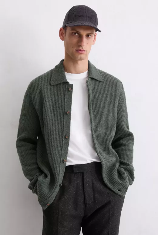 Cardigan vs. Strickjacke – Mann trägt grüne Herren-Strickjacke im Cardigan-Stil über weißem T-Shirt und schwarzer Hose