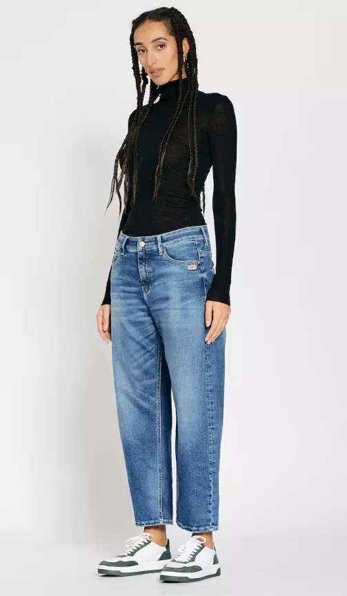 Frau trägt blaue Mom Jeans mit hohem Bund, kombiniert mit schwarzem Rollkragen-Longsleeve und weißen Sneakers mit grünen Details – minimalistischer Casual-Look.