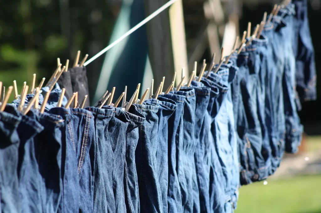 Jeans waschen – mehrere Blue-Jeans auf einer Wäscheleine im Freien, mit Klammern befestigt, lufttrocknen im Schatten.