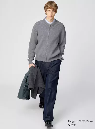 „Model trägt Uniqlo Herren-Outfit mit grauem Strick-Cardigan, blauer Jeans und schwarzen Lederschuhen, kombiniert mit Jacke und Hemd