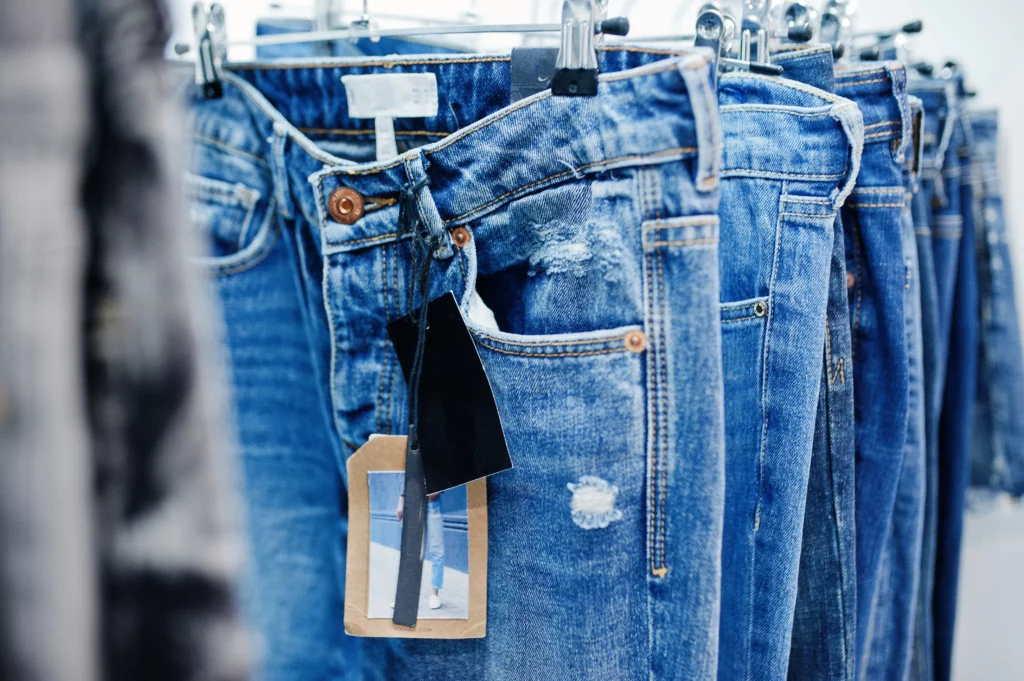 Jeans waschen – hängende Denim-Hosen mit Etiketten, verschiedene Waschungen, Hinweise auf Pflege und Programmwahl.
