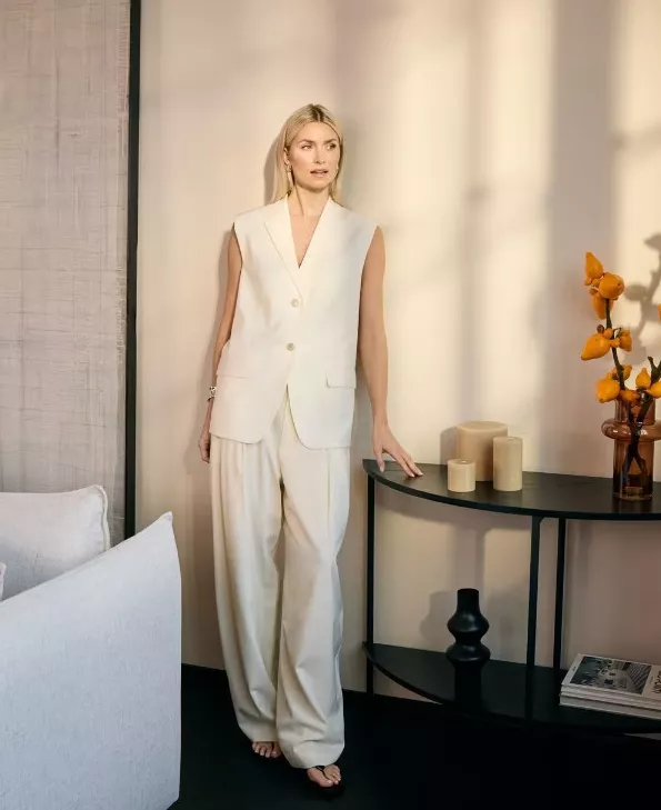Model in cremefarbenem Outfit aus der LeGer Home Kollektion, inszeniert in modernem Interior mit Konsole, Kerzen und Blumen.