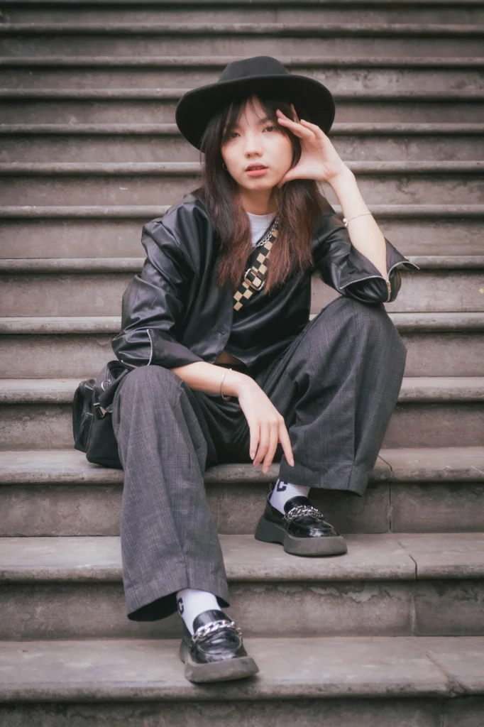 Junge Frau im modernen Korean-Style mit schwarzem Hut und Oversized-Look auf einer Treppe