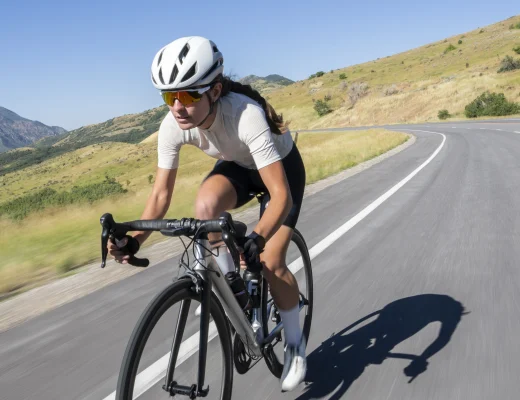 Eine Frau fährt mit ihrem Gravel Bike auf einer Schotterstraße in den Bergen, dynamisch und sportlich, mit Flusstal im Hintergrund.