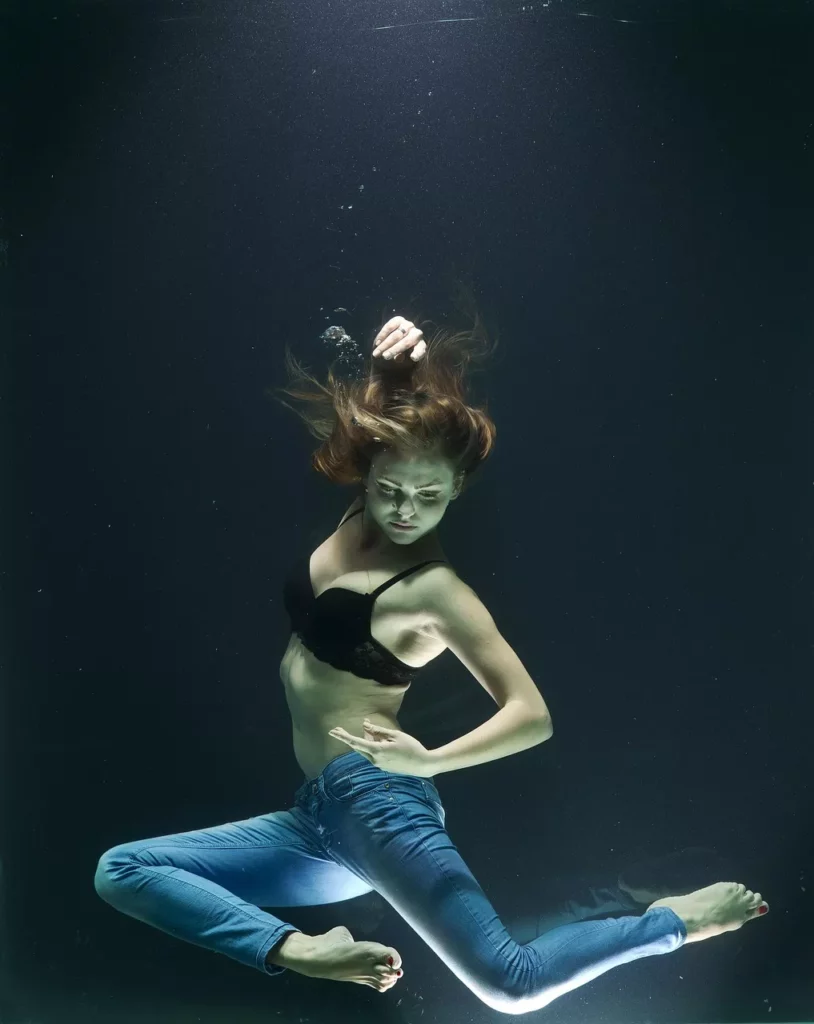 Frau in Low Waist Jeans posiert unter Wasser in dynamischer Bewegung