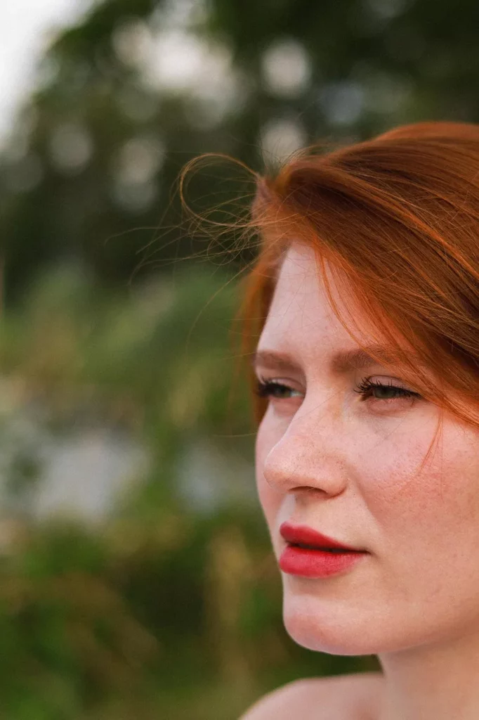 Rote haare bei junger Frau im Porträt, natürlich gestylt mit dezentem Make-up und rotem Lippenstift.