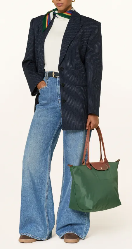 Frau trägt eine grüne Longchamp Le Pliage Tote mit braunen Lederhenkeln; navy Nadelstreifen-Blazer, weißes Top, weite Jeans, buntes Halstuch.