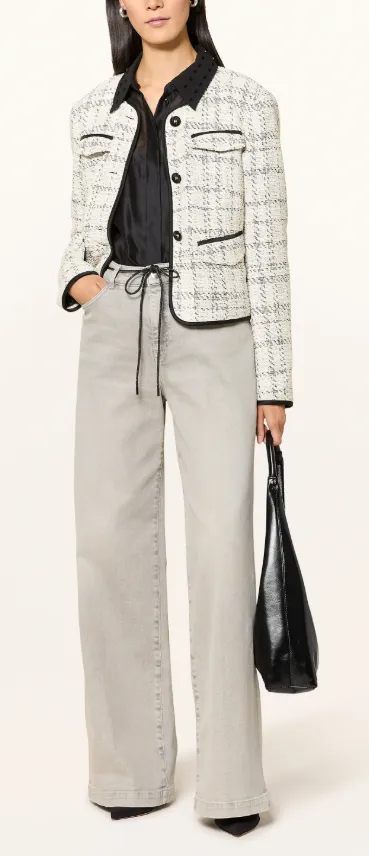 Helle Tweed-Jacke in Schwarz-Weiß mit Kontrastpaspeln, kombiniert mit schwarzer Bluse, grauen Jeans und Tasche – moderner City-Look 2025.