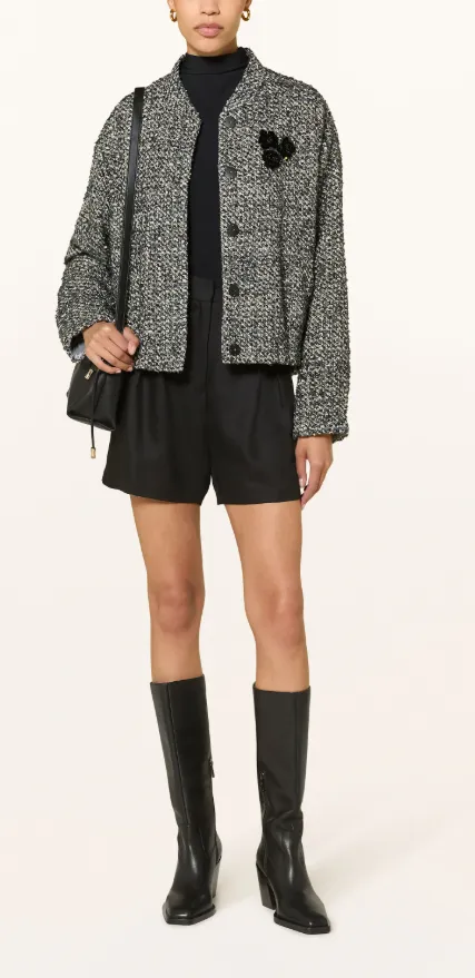 Grauschwarze Tweed-Jacke locker geschnitten, kombiniert mit schwarzem Rollkragen, Shorts, hohen Stiefeln und Schultertasche – moderner Herbstlook.