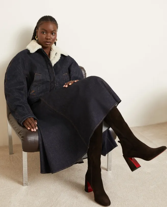 Model im dunkelblauen Denim-Mantel mit Fellkragen trägt kniehohe, dunkelbraune Velourslederstiefel mit Blockabsatz und roter Sohle.
