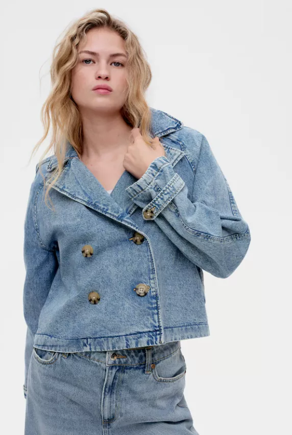 Kurzer Damen-Trenchcoat aus Denim im Boxy-Schnitt, doppelreihig geknöpft, mit Riegeln am Ärmel, kombiniert zu passender Jeans.
