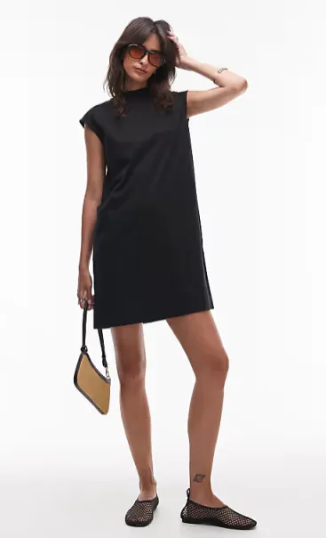 Frau im schwarzen Shift-Minikleid mit Sonnenbrille, Mesh-Ballerinas und kleiner zweifarbiger Tasche – lässiger City-Look.