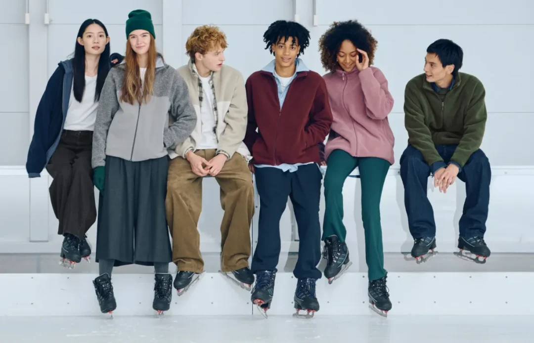 Uniqlo München – junge Menschen in Fleece- und Basics-Looks sitzen mit Eislaufschuhen auf einer Bank in heller Eishalle.