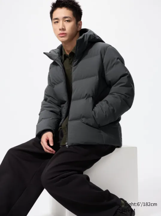 Uniqlo München – Mann trägt dunklegrauen Seamless-Down-Daunenparka, Studioaufnahme im Sitzen.