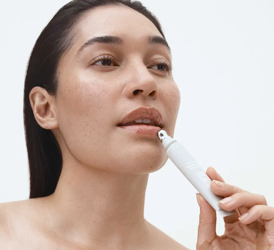 Lippenpflege mit Serum – Frau trägt pflegenden Balm mit kühlender Metallspitze präzise auf die Unterlippe auf, natürliche Haut, Studiohintergrund in Weiß