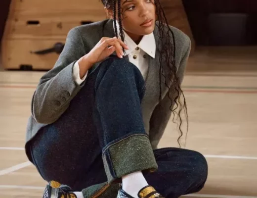GANNI x New Balance 1906L in Fall Leaf/Black/Silver Metallic – Sneaker-Loafer mit Riemendetail und Metallic-Overlays, gestylt zu Blazer, weißem Hemd und Wide-Leg-Denim in einer Sporthalle.